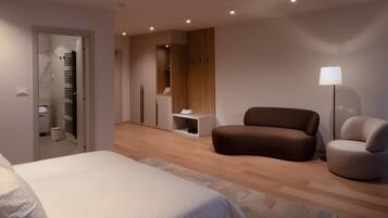 Una habitación de hotel moderna con una cama grande, una zona de estar con dos sofás, un espejo y una mesita.