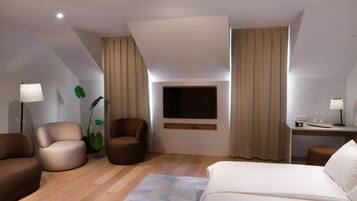 Habitación de hotel moderna con cama, dos sillones, escritorio con lámpara, televisión y una planta grande.