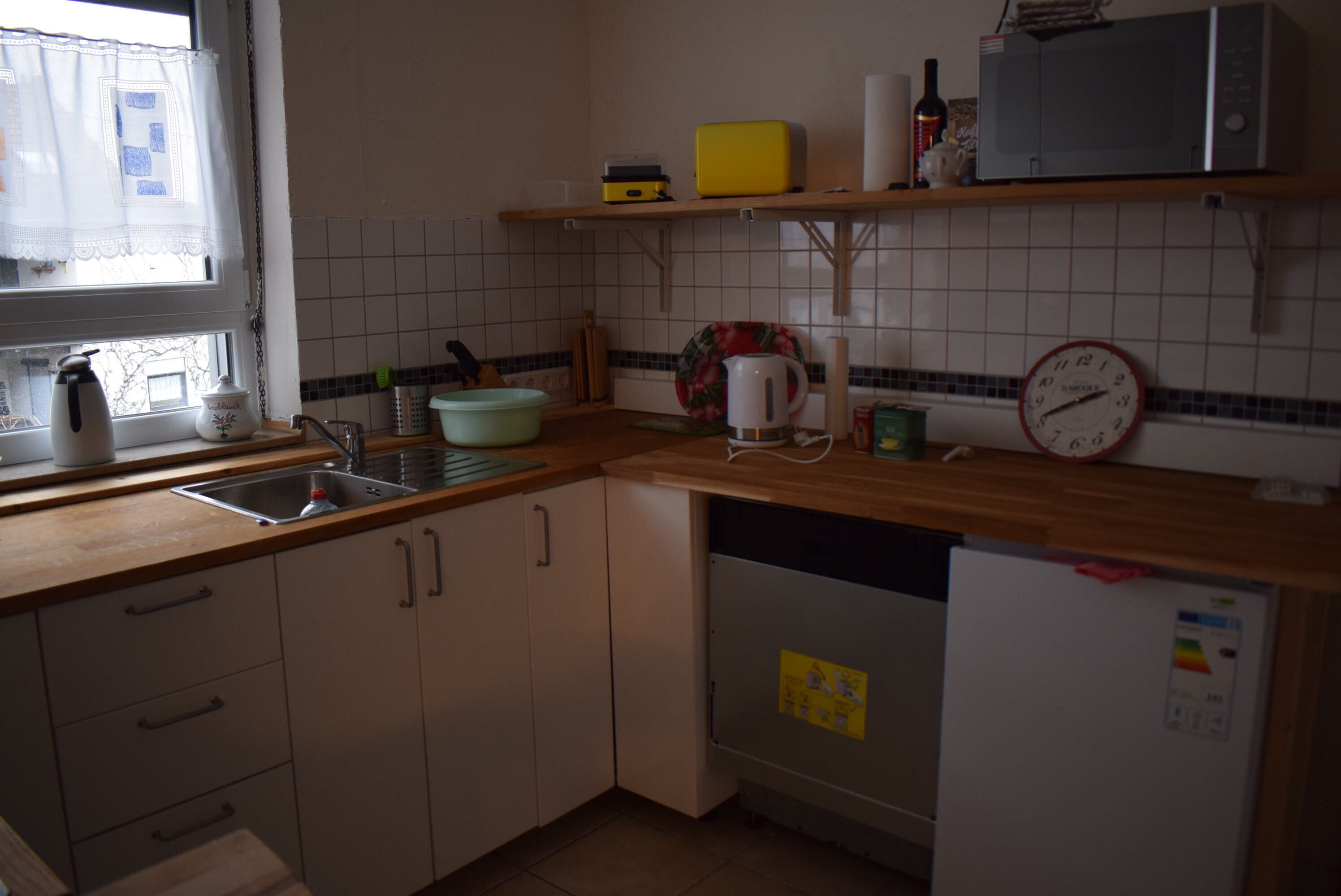 Une cuisine équipée d’un évier, d’un four à micro-ondes, d’une bouilloire et d’une horloge murale.