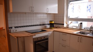 Una cucina con mobili bianchi, una macchina da caffè nera e gialla, un piano di lavoro in legno e una finestra con vista sugli edifici.