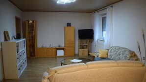 Un soggiorno con un divano, un tavolino in vetro, un televisore su un mobile, un armadio e una libreria.