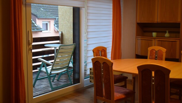 Zona pranzo con tavolo e sedie, una porta scorrevole in vetro che dà su un patio esterno e mobili da cucina in legno.