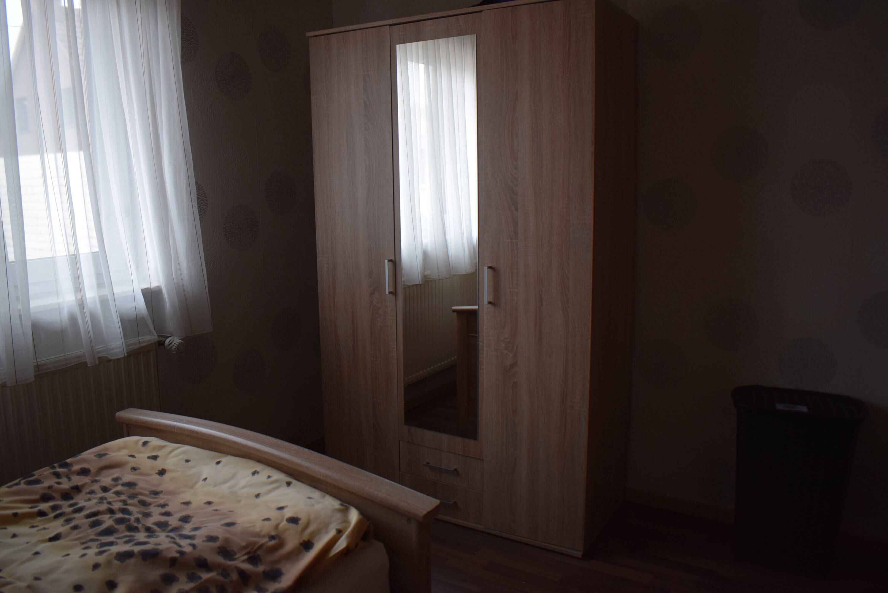 Ein Schlafzimmer mit einem Holzschrank, einem Bett mit gemustertem Überwurf und einem Heizkörper.