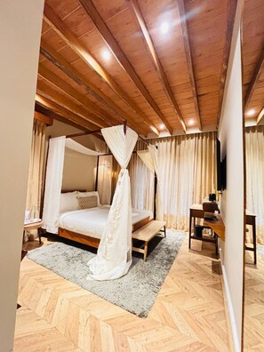 Un dormitorio con cama con dosel, suelo de madera y techo con vigas a la vista.