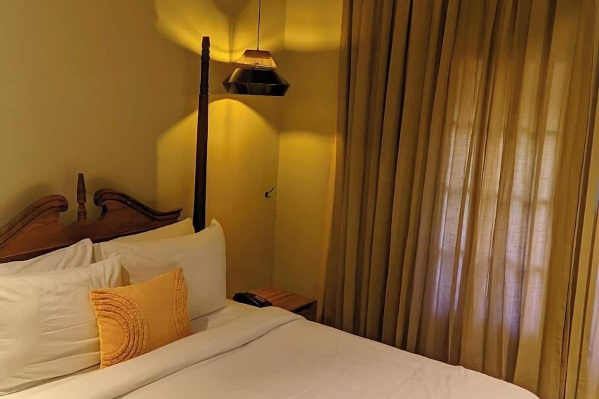 A bedroom with a wooden ceiling, a bed with white bedding, a bench, and a lamp.