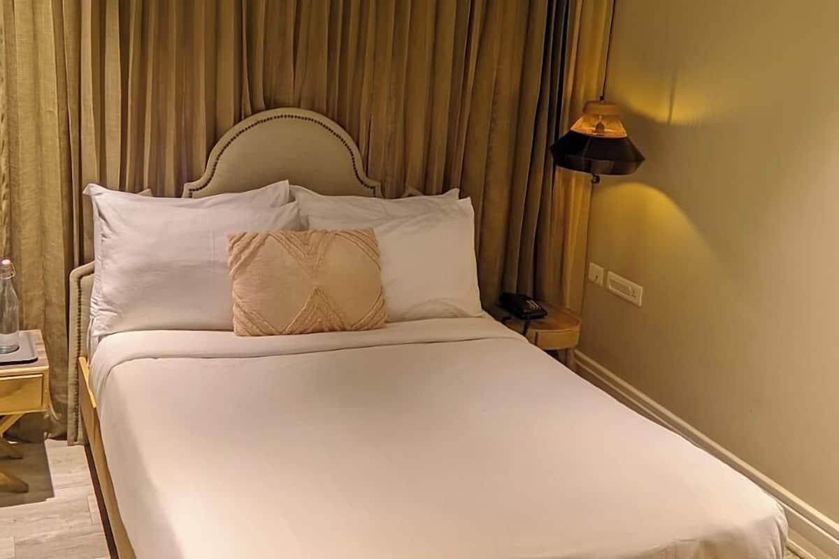 A neatly made bed with a wooden headboard, a bedside table with a lamp, and a bench at the foot of the bed.