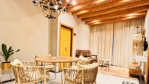A dining area with a wooden table and chairs, a chandelier, and a large window with curtains.