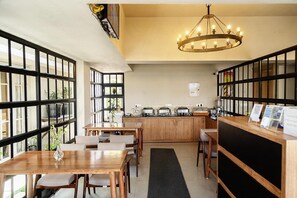 A restaurant with a wooden dining area, a kitchen with pots and a chandelier, and large windows. - Meraki Maison (Ooty)