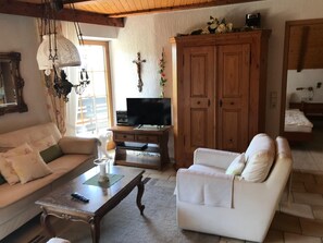 A cozy living room with a sofa, armchair, wooden cabinet, television, and a cross on the wall.