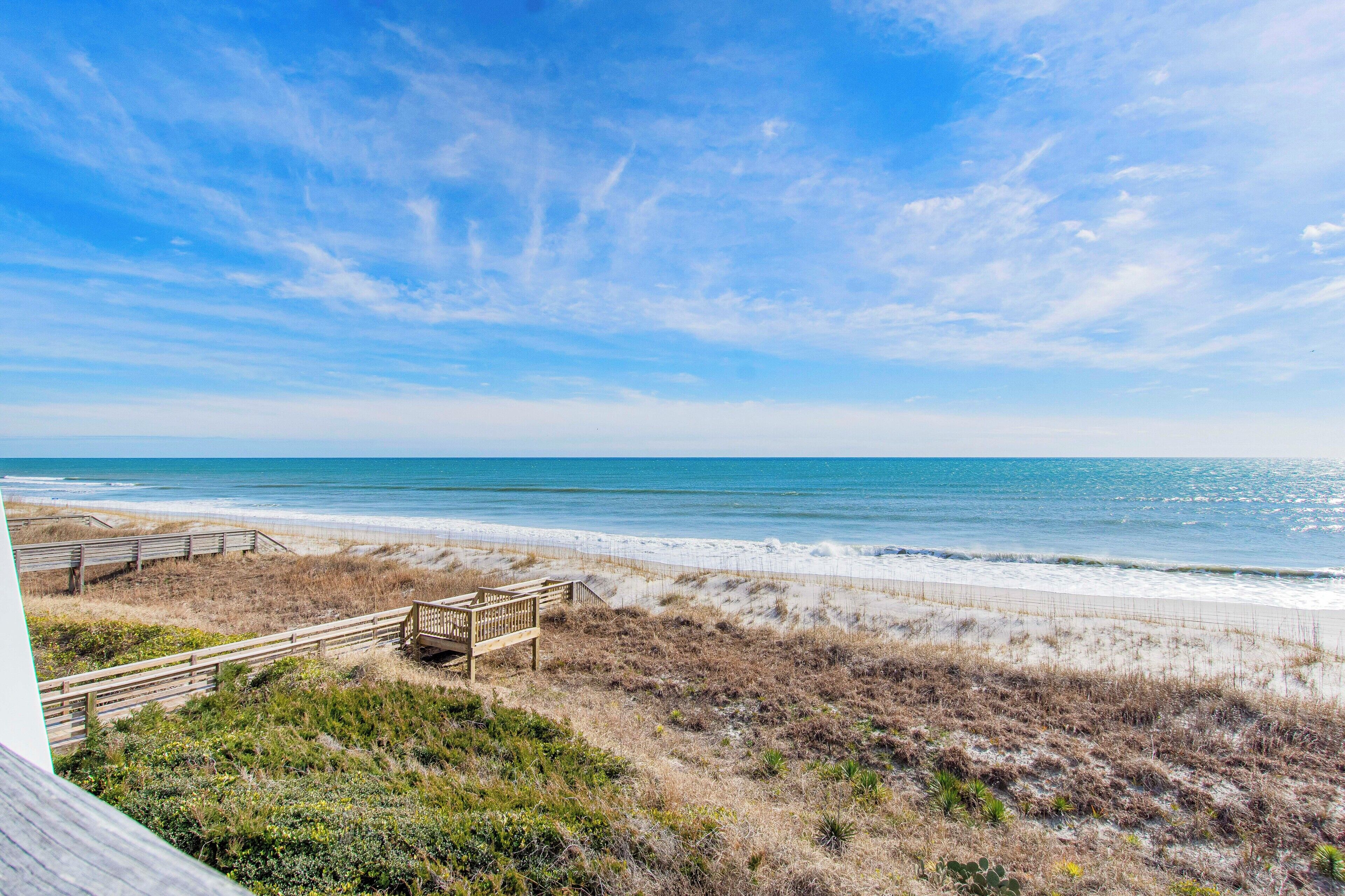 A beach view with a wooden walkway leading to a wooden structure, overlooking the ocean.