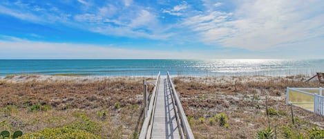 A wooden boardwalk leading to a beach with a clear sky.