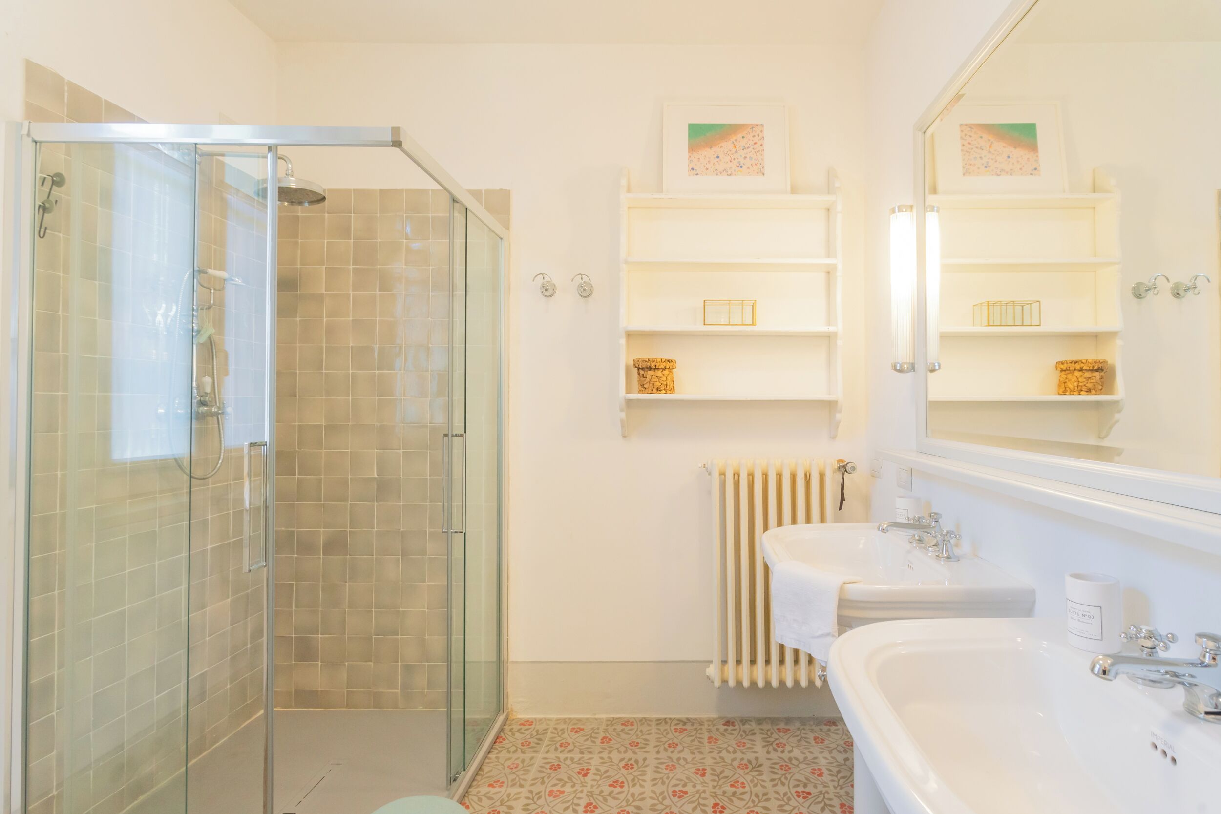 Un bagno con doccia vetrata, due lavandini e uno specchio sopra i lavandini.
