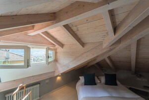 Un dormitorio con techo inclinado, vigas de madera, una cama con almohadas, una ventana y un radiador.