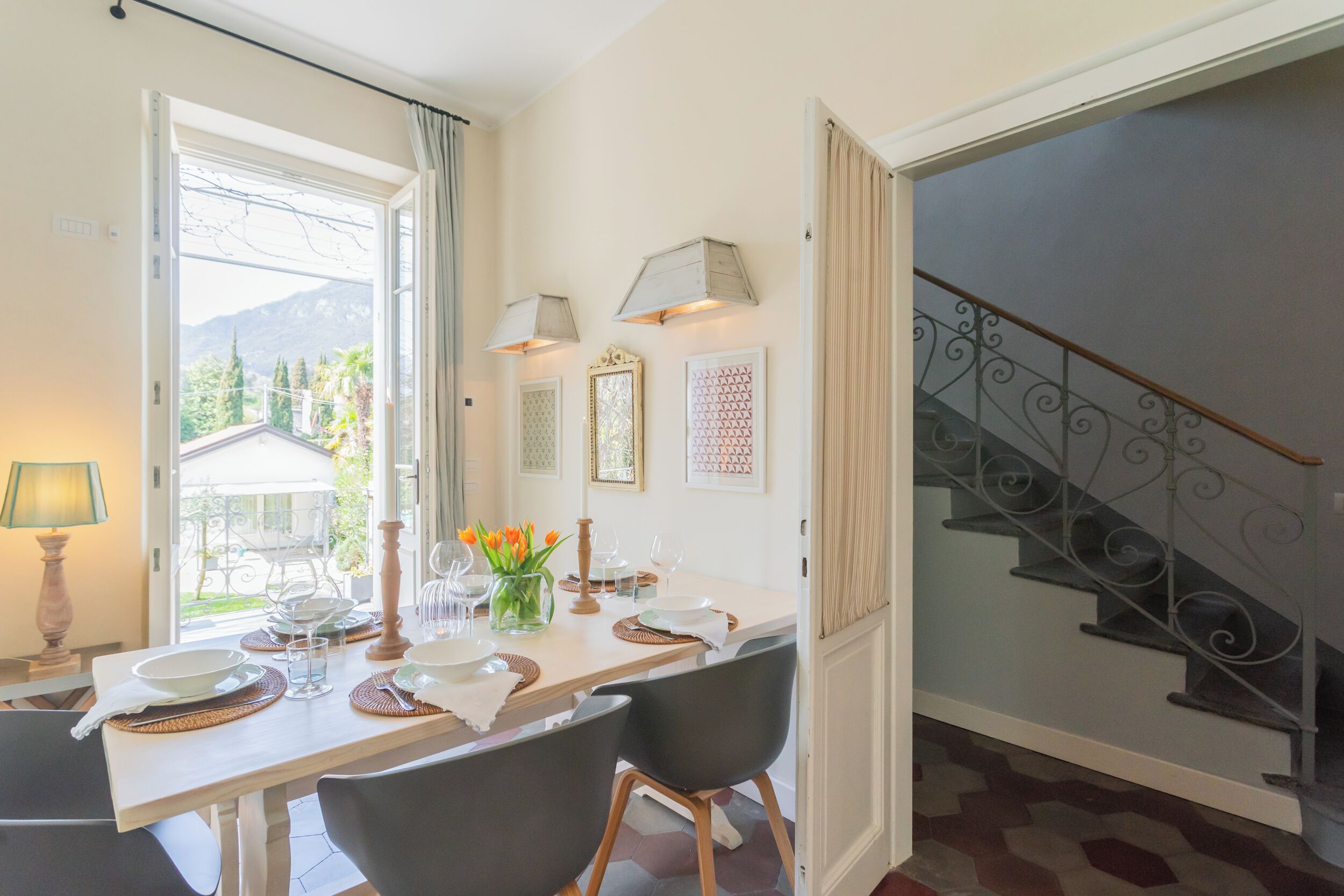 A dining area with a table set for four, a staircase, and a view of greenery outside.