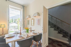 A dining area with a table set for four, a staircase, and a view of greenery outside. - Villa Olga With Private Pool by Rent all Como (Tremezzina)