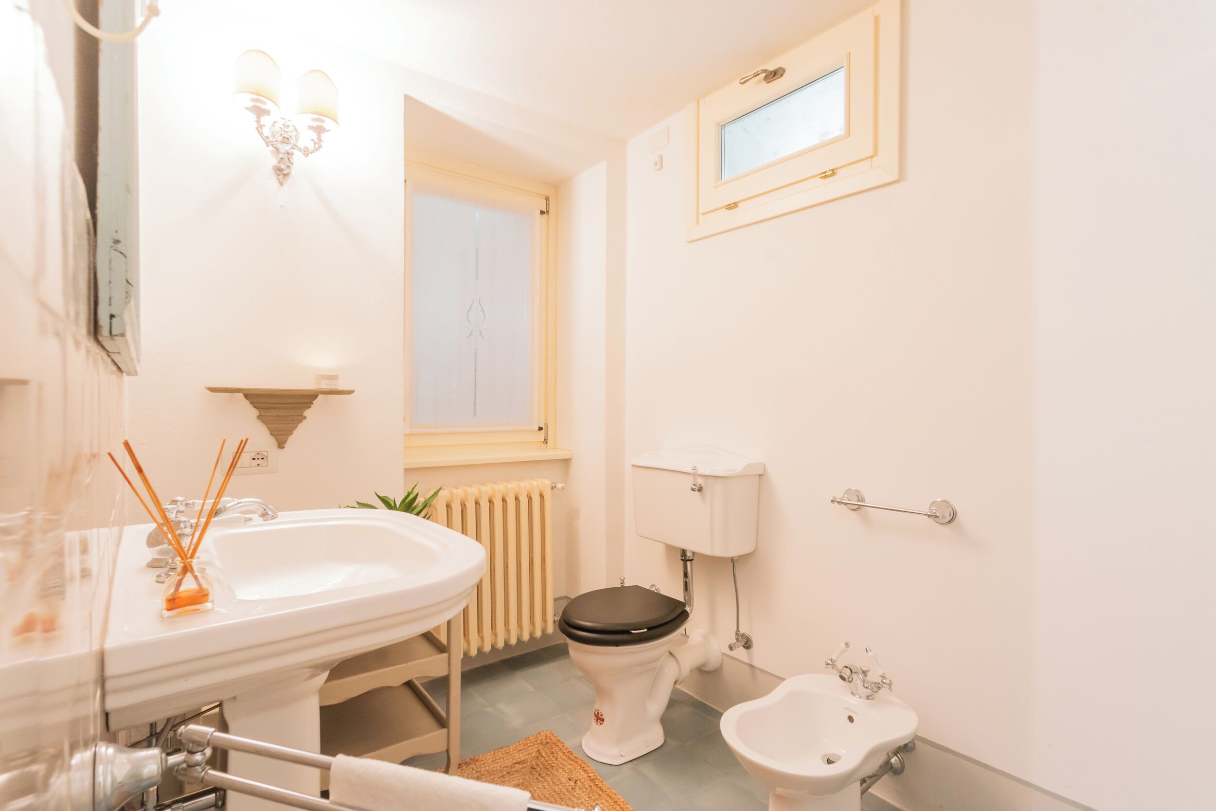 A bathroom with a sink, toilet, bidet, and a small window.