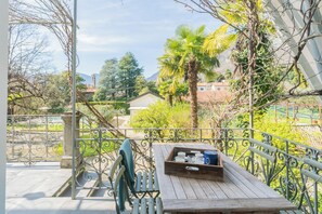 A wooden table with a tray of items on a balcony with wrought iron railings, surrounded by greenery and a view of buildings and mountains. - Villa Olga With Private Pool by Rent all Como (Tremezzina)