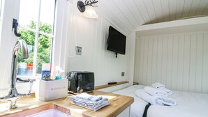 A hotel room with a wooden countertop, a sink, a coffee maker, a TV, and a bed with towels.