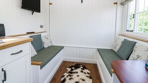 A room with a television mounted on the wall, a wooden bench with a fur rug, and a window with curtains.