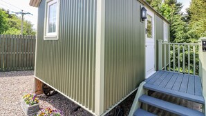 A small, single-story metal building with a curved roof, a small window, and a wooden deck.