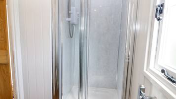A glass-enclosed shower stall with a handheld showerhead and a control panel.