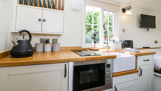 A modern kitchen with white cabinets, a wooden countertop, a kettle, a microwave, and a sink.