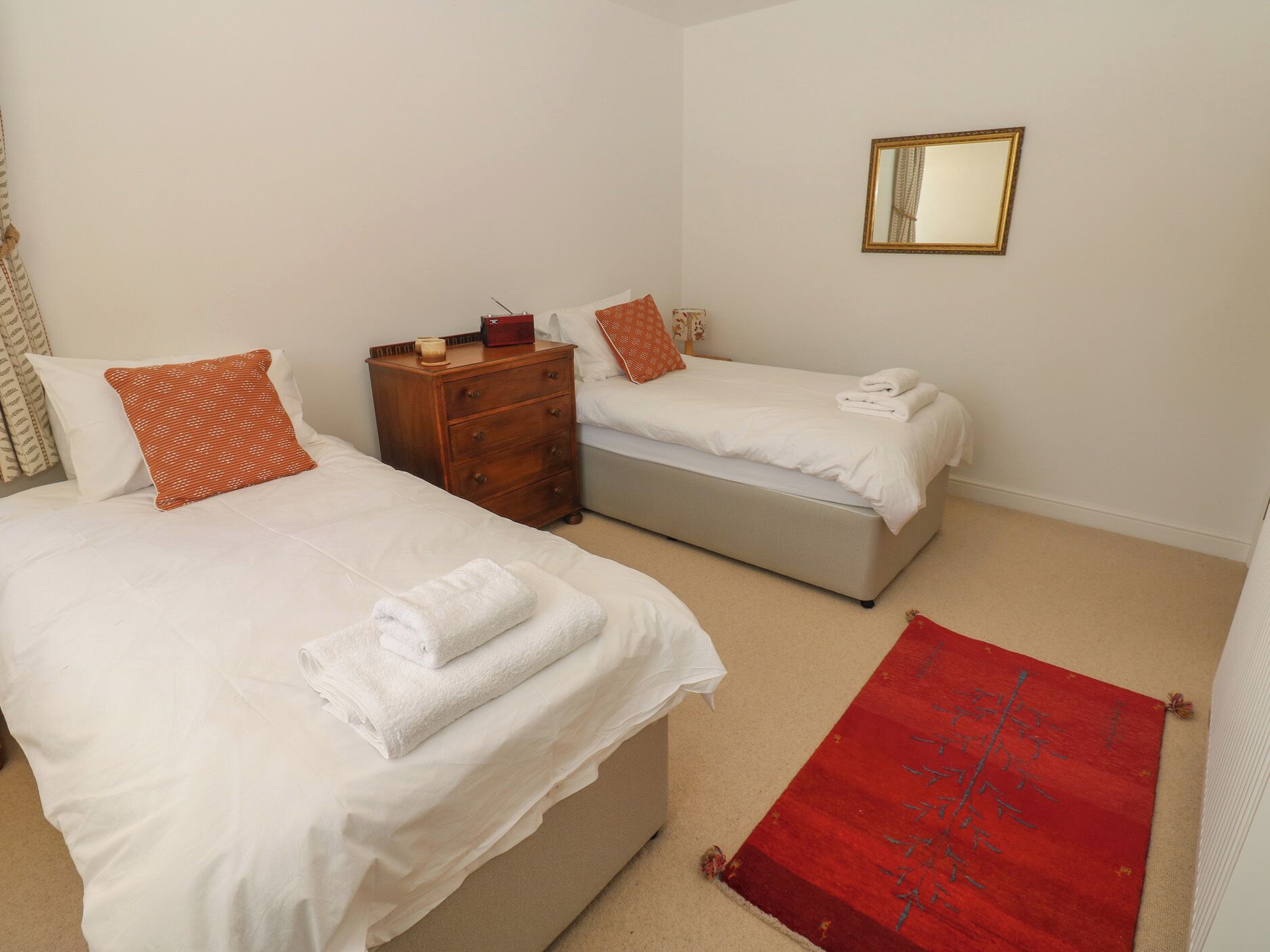 A hotel room with two beds, a wooden nightstand, a red rug, and a mirror on the wall.