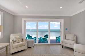A room with a view of the beach, two chairs, a small table, and a window with a view of the ocean. - Beachfront Retreat w/ Panoramic Views and Pool (Madeira Beach)