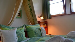 Ein Bett mit grün-weißer Bettwäsche, einem Holz-Kopfteil, einem Nachttisch mit Lampe und einem fenster mit Vorhängen.