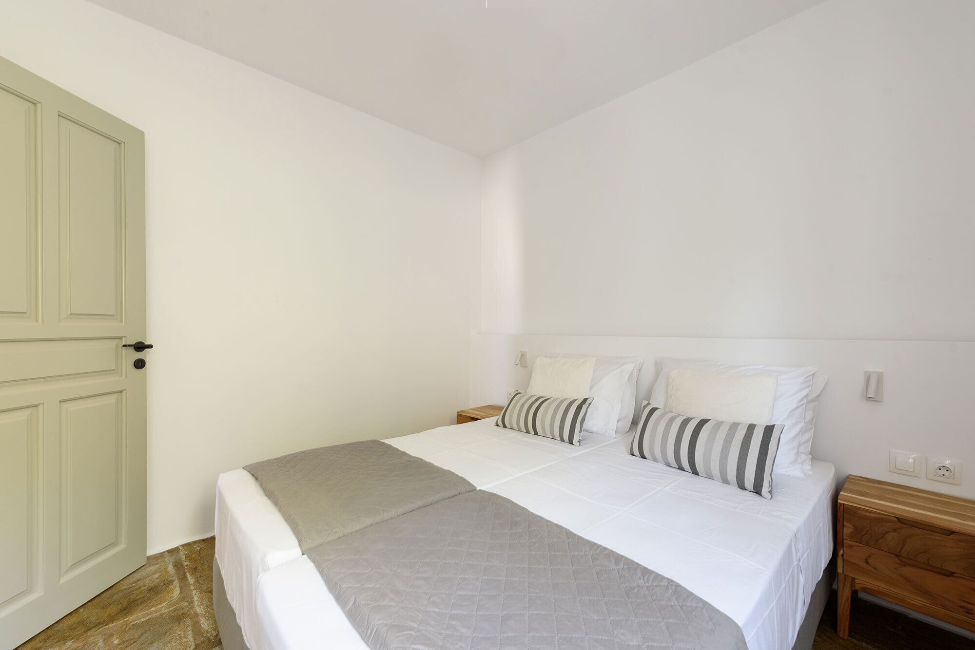 Ein Schlafzimmer mit einem Bett, einem Nachttisch, einer Tür und einem Lichtschalter an der Wand.