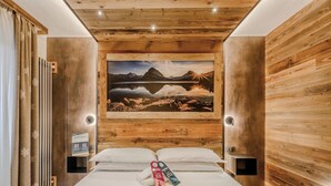 A hotel room with a wooden ceiling, a bed with white linens, a framed landscape painting, and a bedside table with a lamp. - Hotiday Sauze Centro (Sauze d'Oulx)