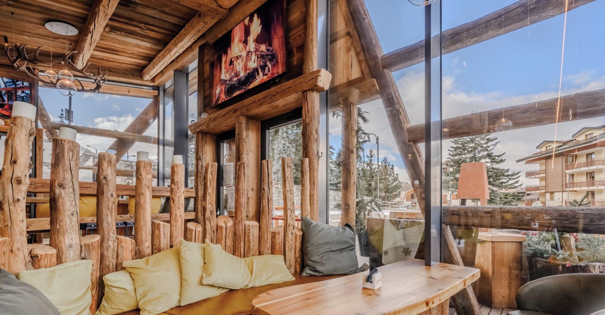 A rustic wooden interior with a fireplace, wooden beams, and a view of the outside.