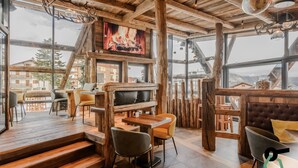 Un interior rústico de madera con chimenea, zona de estar y ventanas amplias que ofrecen vistas de los edificios circundantes.