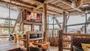 Un interior rústico de madera con chimenea, zona de estar y ventanas amplias que ofrecen vistas de los edificios circundantes.