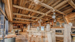Interior rústico de madera con una zona de bar, asientos y vistas al exterior.