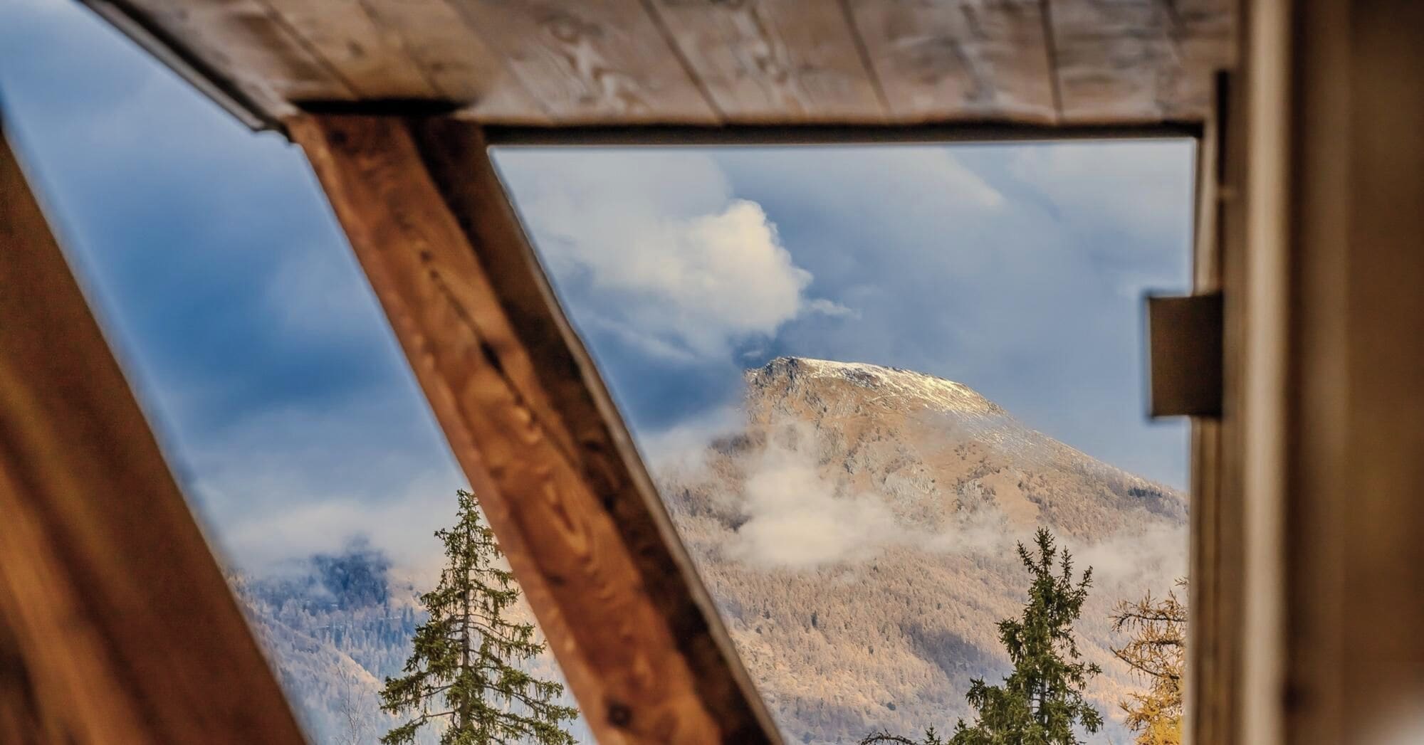 A mountain view through a wooden-framed window, with trees in the foreground.
