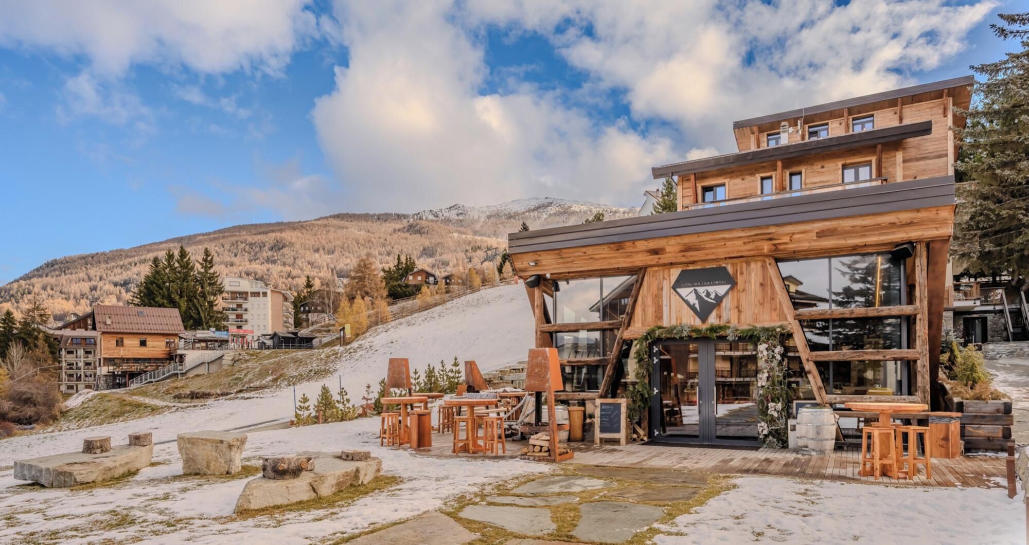 Un chalet en bois doté d’une terrasse en pierre, entouré de neige et de montagnes.