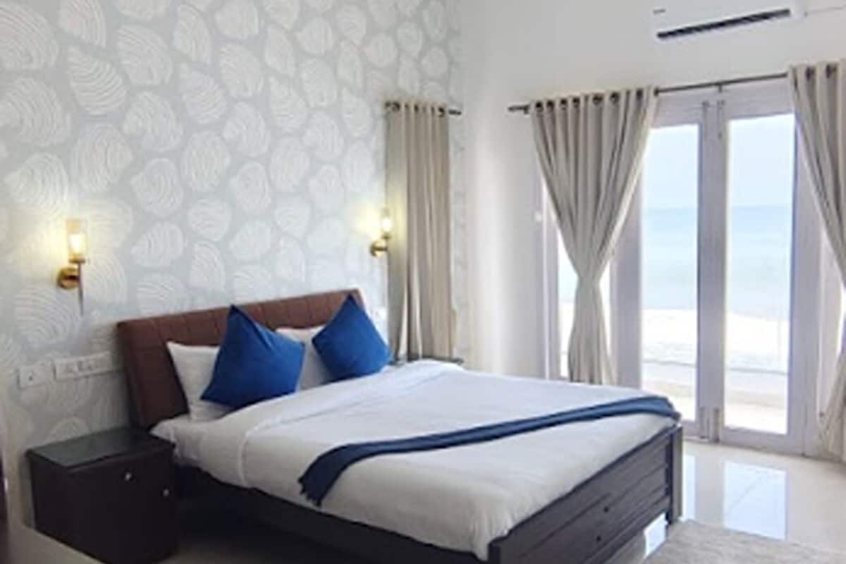 Een slaapkamer met een bed, nachtkastjes, een plafondventilator en uitzicht op de zee door grote ramen.