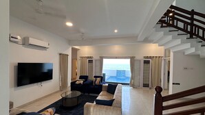 Un salon moderne doté d’un téléviseur à écran plat, d’un ensemble de canapés, d’une table basse et offrant une vue sur la mer grâce à de grandes fenêtres.