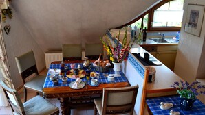 A dining area with a checkered tablecloth, chairs, a vase with flowers, and a view of a kitchen through an archway. - Apartment 'Schwalbennest' with Mountain View, Private Balcony and Wi-Fi (Sasbachwalden)
