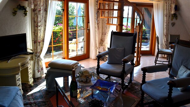 A cozy living room with a television, a wooden chair, a sofa, and a glass coffee table. - Apartment 'Schwalbennest' with Mountain View, Private Balcony and Wi-Fi (Sasbachwalden)