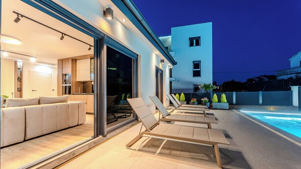 A modern outdoor living area with a pool, lounge chairs, and a dining area with a sofa and table. - Villa Ballat (Privlaka)