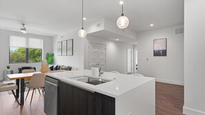 A modern kitchen with a central island, pendant lighting, and a dining area with a table and chairs.