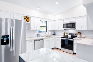 A modern kitchen with white cabinetry, stainless steel appliances, a built-in dishwasher, and a marble countertop.