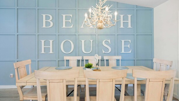 A dining area with a table and chairs, a chandelier, and a wall with large letters spelling "BEACH HOUSE". - 3BR Coastal Home Near Beach w/ Fire Pit (St. Augustine)