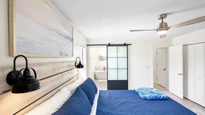A bedroom with a bed, a ceiling fan, a wall-mounted lamp, and a sliding door leading to a bathroom. - 3BR Coastal Home Near Beach w/ Fire Pit (St. Augustine)