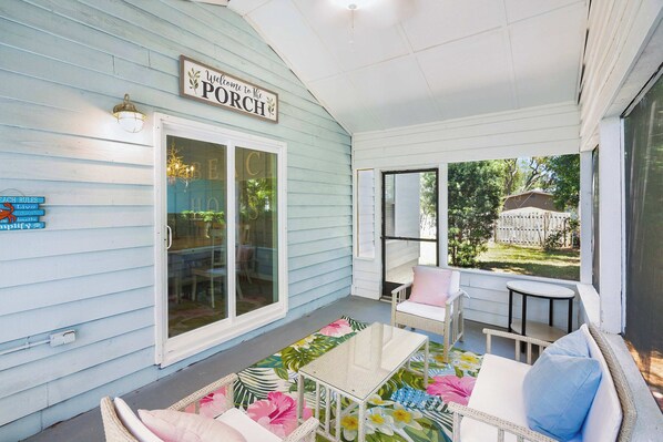 A covered porch with a 'Welcome to the Porch' sign, wicker furniture, and a view of a backyard.