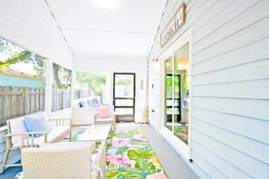 A covered porch with wicker furniture, a floral floor mat, and a welcoming sign.