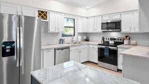 A modern kitchen with white cabinets, stainless steel appliances, and a marble countertop. - 3BR Coastal Home Near Beach w/ Fire Pit (St. Augustine)