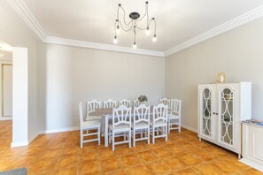Un comedor con una mesa y sillas blancas, una araña y un aparador con puertas de cristal.